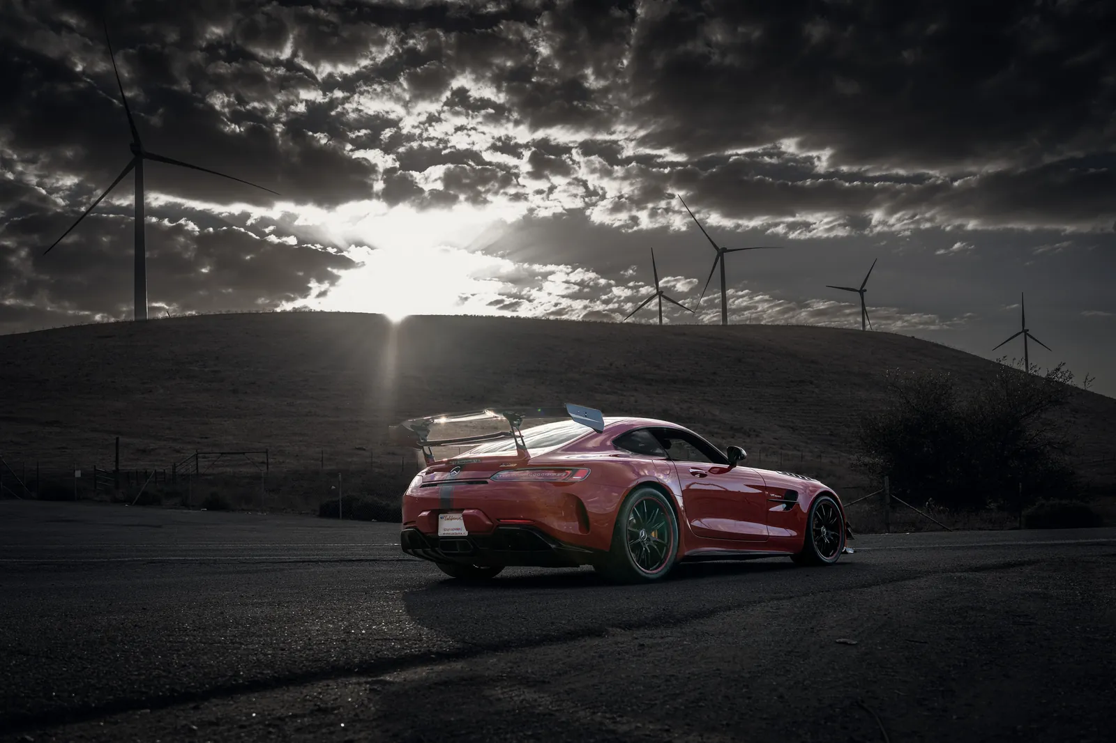 Mercedes-AMG GT R below wind turbines, the sun breaking through dark clouds
